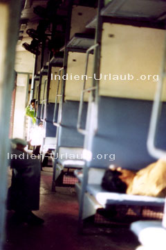 Indien Bahnreisen in der 2. Klasse. Man sieht auf dem Bild das Zugabteil mit den Sitzplätzen und 3 Inder.