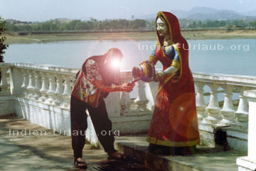 Ein Tourist der sich bei den Indien Reisen an einem Brunnen erfrischt wo das Wasser von einer indischen Göttin ohne Unterlass aus einem Krug sprudelt.
