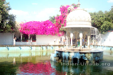 Touristen die die leuchtende Blumenpracht und ein See mit Springbrunnen hinter dem Pavillon in einem der vielen Paläste in der Old City von Udaipur im indischen Bundesstaat Rajasthan besichtigen.